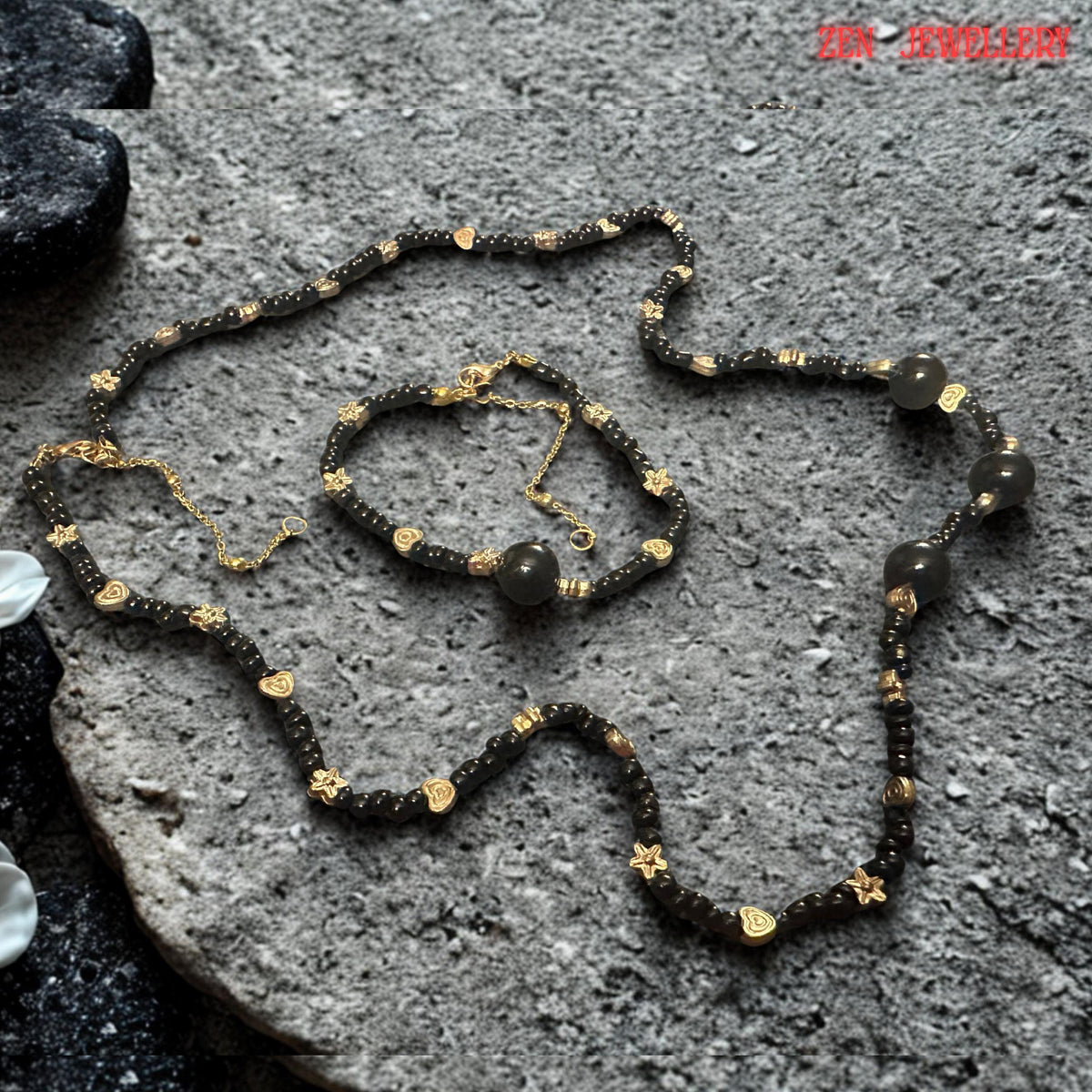 The jewellery set is photographed against a natural stone-inspired surface that complements the organic beauty of the black agate gemstones. The neutral grey tones provide excellent contrast, allowing the deep black beads and warm gold details to stand out clearly. This styling demonstrates how the jewellery combines bohemian influences with refined elegance suitable for both everyday outfits and special occasion wear.