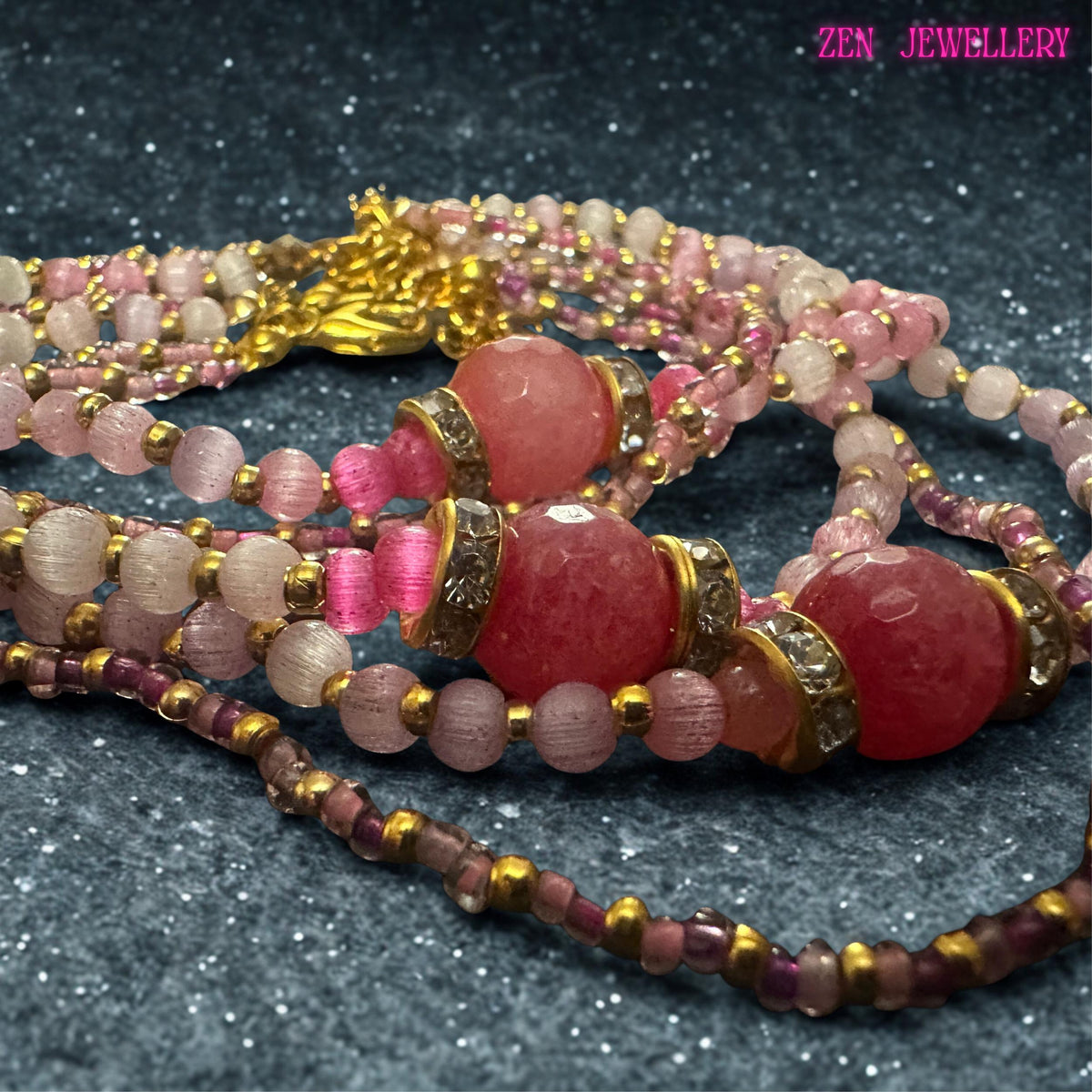 The layered bracelet combines several coordinated strands to create a fashionable stacked jewellery effect. Light pink quartz beads are spaced with gold accents while miniature seed beads introduce extra texture and visual detail. The larger raspberry focal bead stands out against the softer pastel tones and reflects light through its faceted surface. Bracelet length is approximately 21 cm and includes an extender chain for additional adjustment.