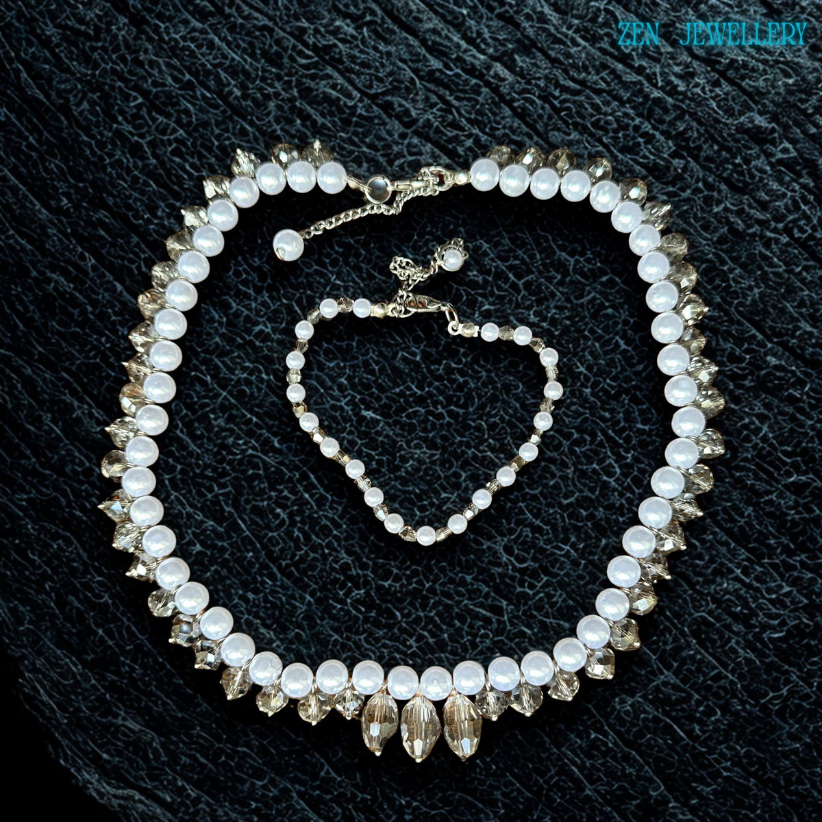 Elegant white pearl and crystal necklace set photographed flat on a textured black surface showing the detailed bead arrangement and sparkling crystal reflections. The necklace combines classic pearl beauty with modern crystal styling while the bracelet complements the design with matching white beads and silver details. The soft glossy finish gives the jewellery a luxurious and graceful appearance suitable for weddings parties and meaningful gif