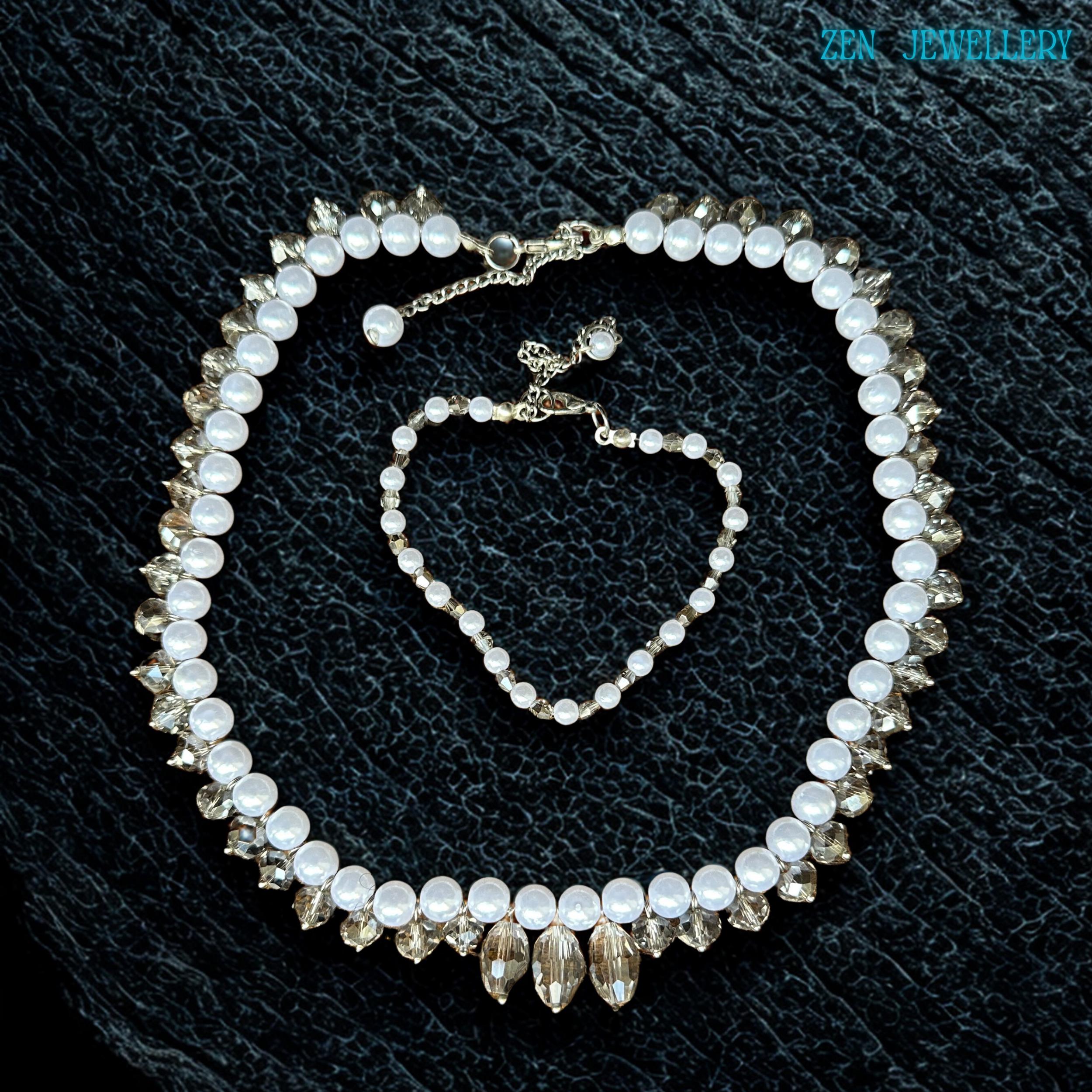 Elegant white pearl and crystal necklace set photographed flat on a textured black surface showing the detailed bead arrangement and sparkling crystal reflections. The necklace combines classic pearl beauty with modern crystal styling while the bracelet complements the design with matching white beads and silver details. The soft glossy finish gives the jewellery a luxurious and graceful appearance suitable for weddings parties and meaningful gif