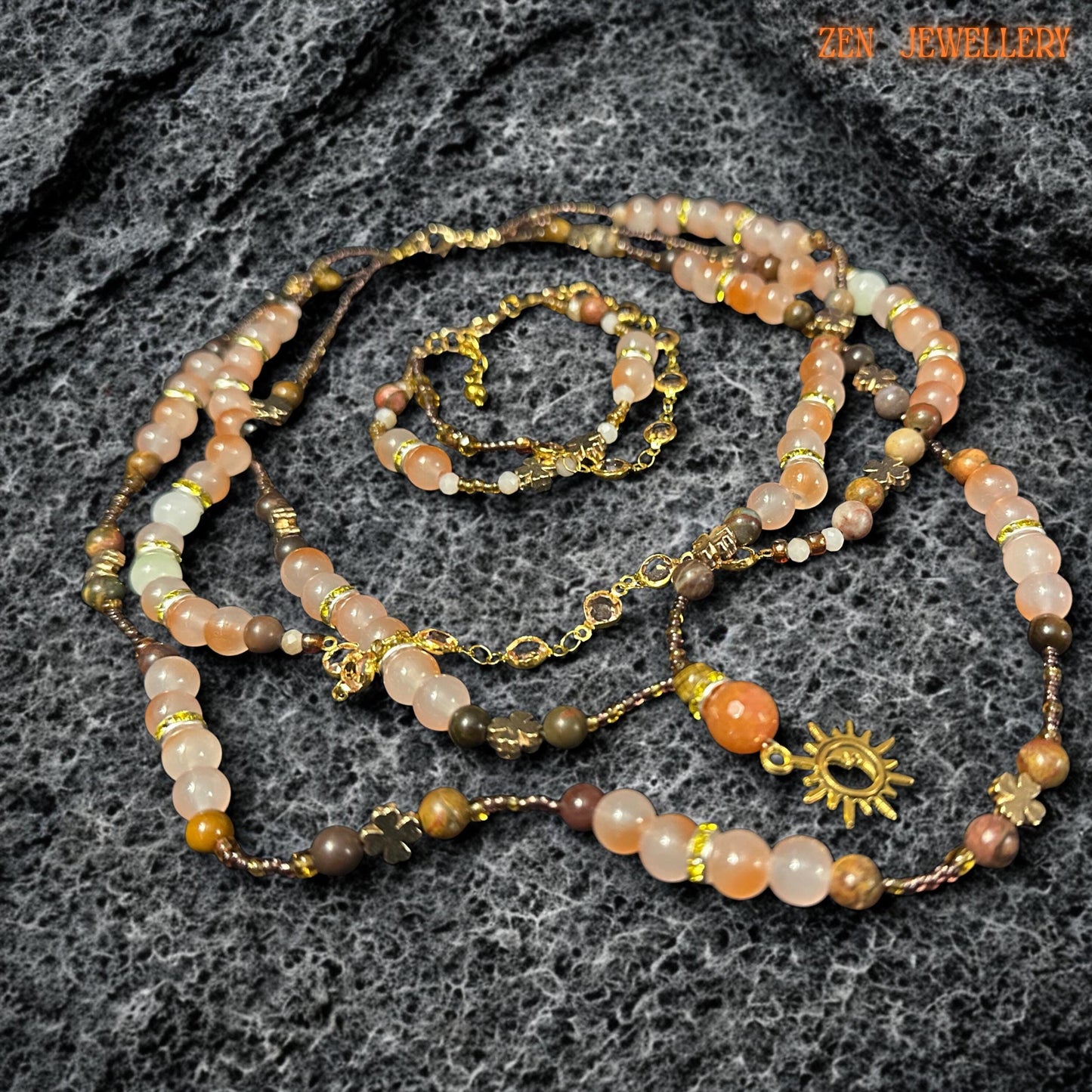 Warm tone gemstone necklace and bracelet set photographed on dark volcanic style stone surface featuring soft peach aventurine, earthy jasper tones, champagne crystal beads, and polished amber inspired details. Faceted crystal beads add subtle sparkle while round gemstone beads create smooth luxurious texture. Adjustable gold clasp and delicate chain extender provide comfortable fit and elegant finish.
