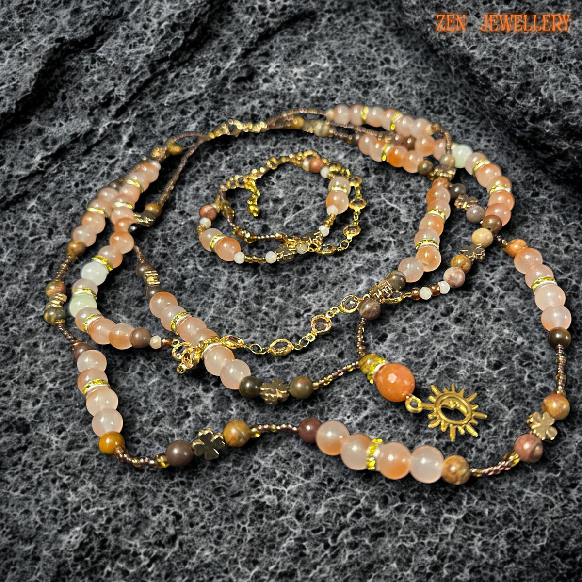 Warm tone gemstone necklace and bracelet set photographed on dark volcanic style stone surface featuring soft peach aventurine, earthy jasper tones, champagne crystal beads, and polished amber inspired details. Faceted crystal beads add subtle sparkle while round gemstone beads create smooth luxurious texture. Adjustable gold clasp and delicate chain extender provide comfortable fit and elegant finish.