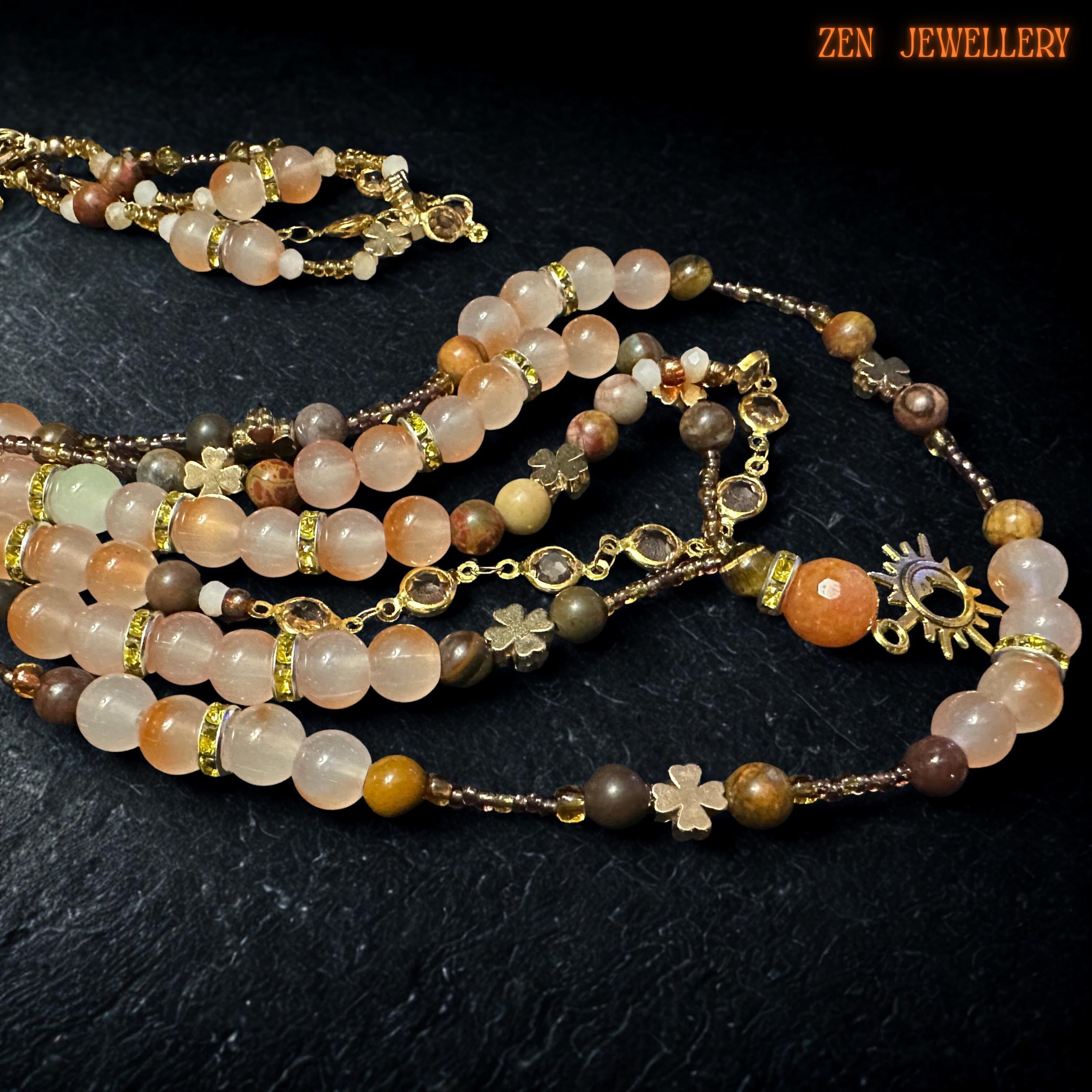 Feminine gemstone necklace with layered strands of peach aventurine, honey beige crystals, earthy brown gemstone beads, and champagne faceted accents displayed against a textured black stone background. Gold spacer beads separate polished stones beautifully while celestial pendant and delicate chain details create a romantic bohemian aesthetic with elegant handcrafted finish.