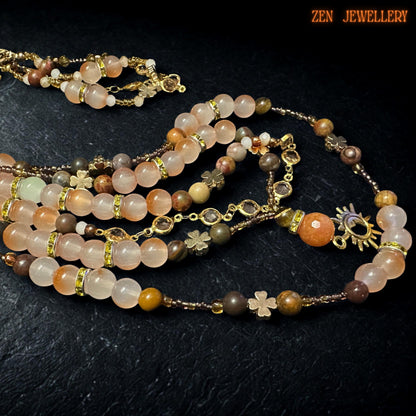 Feminine gemstone necklace with layered strands of peach aventurine, honey beige crystals, earthy brown gemstone beads, and champagne faceted accents displayed against a textured black stone background. Gold spacer beads separate polished stones beautifully while celestial pendant and delicate chain details create a romantic bohemian aesthetic with elegant handcrafted finish.