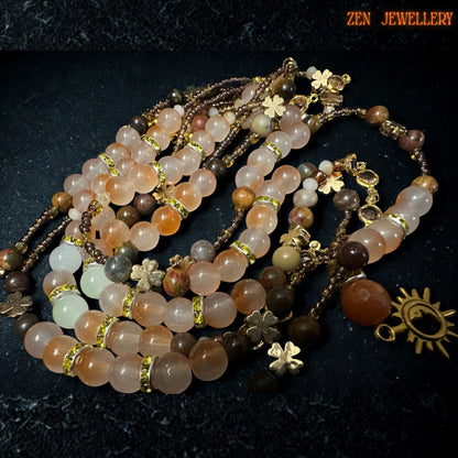 Detailed close-up photograph of elegant layered aventurine jewellery set showing polished round gemstone beads with smooth glossy texture and soft earthy colouring. Champagne crystal beads reflect warm golden light while gold spacer details and celestial sun pendant create luxurious boho style. Necklace includes layered 42 cm, 44 cm, and 51 cm strands with matching adjustable bracelet.