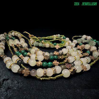 • Handmade layered necklace with soft earthy gemstone tones including pale green aventurine, ivory crystal beads, creamy jade style stones, and dark green striped accents displayed on a textured charcoal stone background. The faceted metallic beads catch light beautifully while the celestial gold sun charm adds mystical elegance and artistic detail to the bohemian jewellery set.