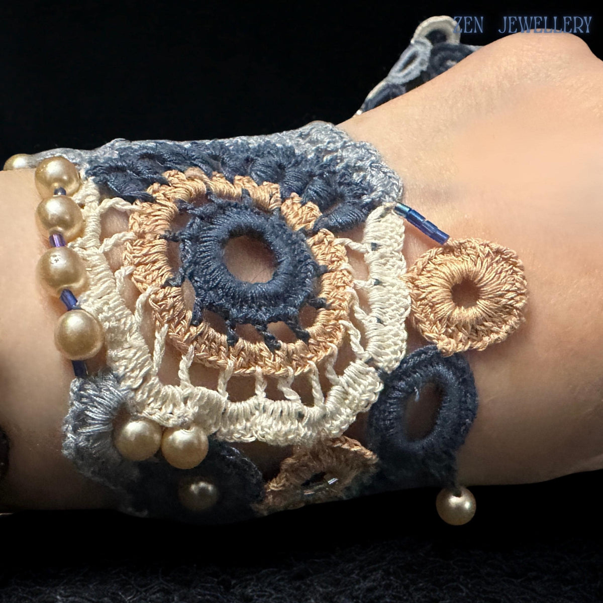 Matching crochet bracelet featuring embroidered cotton circles, delicate pearl accents and sculptural textile artistry displayed on a dark textured fabric surface to emphasise the contrast between the soft handmade fibres and luminous pearl embellishments in elegant bohemian luxury style.