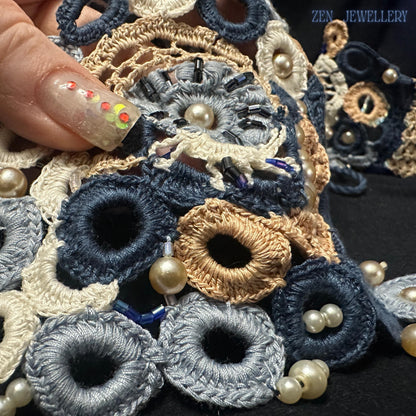 Luxury artisan crochet jewellery designed with interconnected embroidered loops and floral lace elements featuring soft dusty blue and ivory tones combined with white pearls and sculptural textile forms creating a unique statement necklace and bracelet set for women who love wearable fibre art.