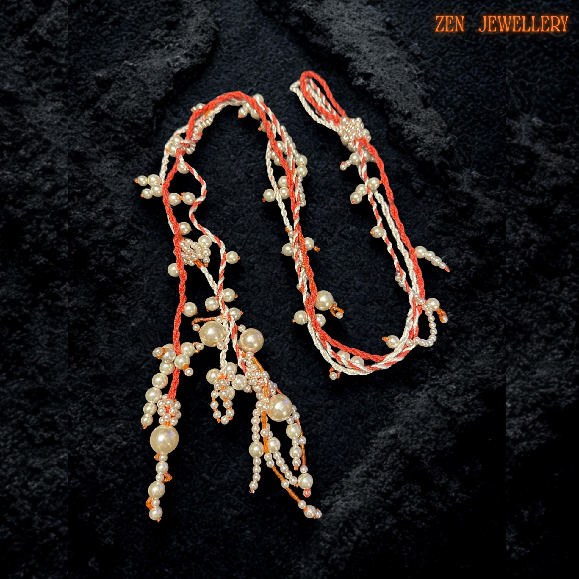 Close-up image highlighting detailed WHITE PEARL beadwork attached carefully onto coral orange crochet strands with handcrafted precision. The necklace features flowing pearl tassels with mixed bead sizes arranged along soft textile cords to create movement and depth. Tiny ivory and orange seed beads add subtle detail and texture while the asymmetrical silhouette creates a modern artistic appearance.
