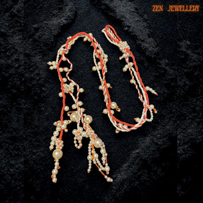Close-up image highlighting detailed WHITE PEARL beadwork attached carefully onto coral orange crochet strands with handcrafted precision. The necklace features flowing pearl tassels with mixed bead sizes arranged along soft textile cords to create movement and depth. Tiny ivory and orange seed beads add subtle detail and texture while the asymmetrical silhouette creates a modern artistic appearance.
