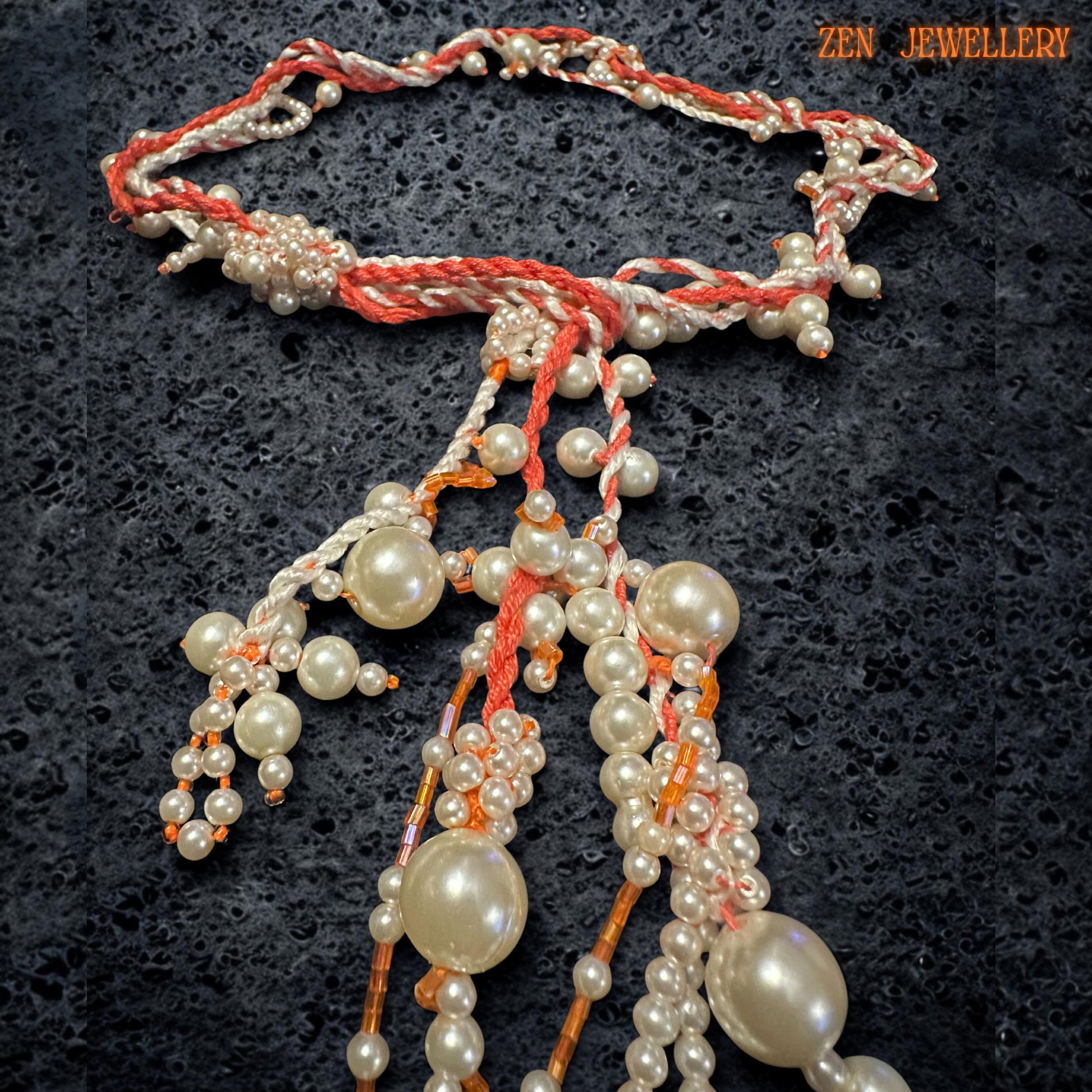 Handmade pearl statement necklace featuring elegant ivory pearl beads suspended from warm coral crochet strands with flowing layered tassel details. The asymmetrical arrangement creates sculptural movement and artistic texture while the delicate seed beads add handcrafted refinement. The soft cream and coral colour palette gives the necklace warmth, femininity, and romantic bohemian character.