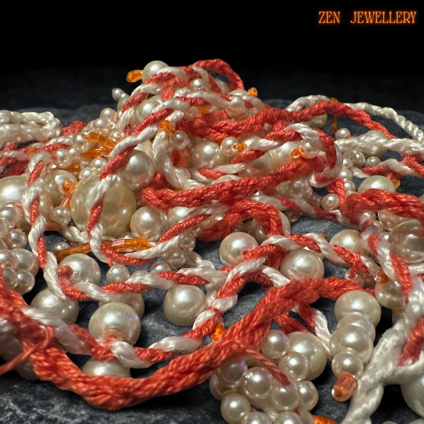 Artistic WHITE PEARL jewellery design shown from above to reveal the sculptural layered tassel arrangement and handcrafted crochet structure. The necklace features flowing ivory pearl strands attached onto twisted coral textile cords with delicate seed bead accents throughout the design. Larger pearl drops add visual depth while the asymmetrical silhouette creates graceful movement and modern bohemian elegance.