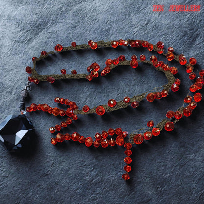 Elegant handcrafted crystal necklace with fiery red faceted stones woven along black crochet strands for a dramatic feminine look. The varied crystal sizes create layered texture and reflective sparkle while the flowing asymmetrical arrangement adds movement and artistic expression. The soft textile structure gives the necklace flexibility and comfort despite its bold statement appearance. The contrast of rich crimson shine and dark braided textu