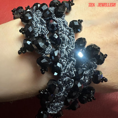 Elegant black crystal crochet jewellery photographed with dramatic lighting to showcase the sparkle of faceted beads and the texture of charcoal silk thread. The handcrafted necklace and bracelet set features dimensional bead clusters that resemble floral or organic formations along the crochet base. The dark monochrome palette gives the jewellery a timeless evening style ideal for pairing with black dresses, minimalist outfits, or alternative fa