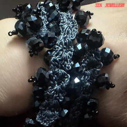 Bold black crystal necklace bracelet set handmade using crochet techniques and charcoal silk thread with sterling silver clasps. The large faceted crystals create a luxurious eveningwear statement while the crochet structure softens the look with artistic texture. The jewellery is styled casually in the hand to show wearability, flexibility, and approximate size. The monochrome colour palette creates a chic, modern gothic aesthetic suitable for e