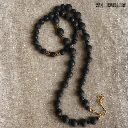 Black volcanic stone necklace and bracelet set photographed together to showcase the handcrafted arrangement of natural lava beads and golden decorative spacer details. The matte black stones create depth and texture while the gold accents brighten the design and add luxury to the earthy volcanic jewellery aesthetic.