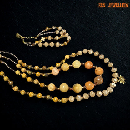 Close-up image of the gold clasp and adjustment area showing polished finishing details and secure handmade construction. The celestial charm pendant adds a delicate symbolic touch to the design.
Warm golden gemstone necklace with matching bracelet arranged in a circular display. The beads reflect light softly, creating an elegant, earthy, and feminine appearance inspired by boho luxury styling.