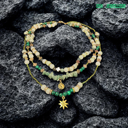 • Handmade bohemian gemstone necklace and bracelet set featuring natural aventurine stones, creamy crystal beads, floral spacer charms, and delicate gold details arranged beautifully on a textured black stone surface. The rich contrast between the dark background and soft green gemstones highlights the elegant handcrafted finish and the artistic layered structure of the jewellery set.
