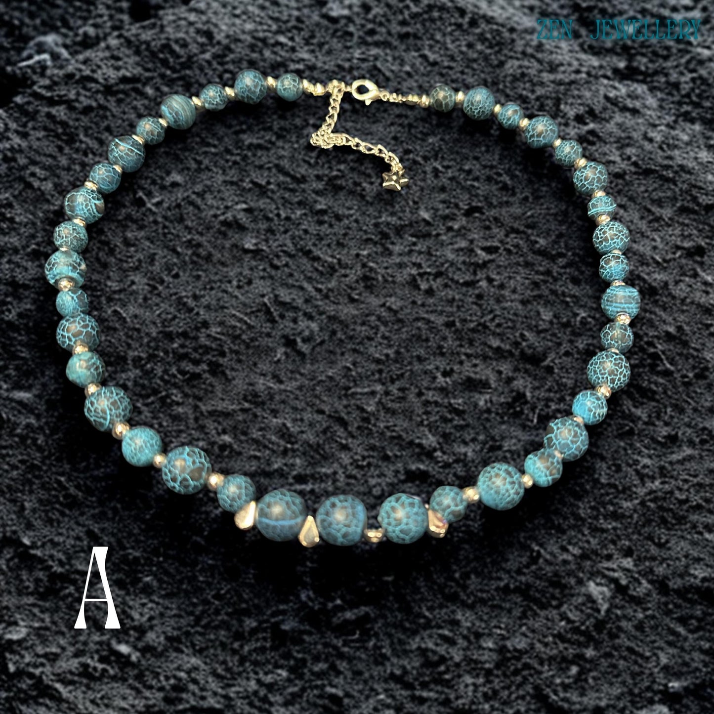 Close-up image of Blue Crackle Agate gemstone beads showing detailed crackled vein textures in deep turquoise, black, and ocean blue shades separated by polished silver spacer beads that reflect light softly against the dark background, highlighting the natural stone patterns, handcrafted jewellery construction, layered bead arrangement, and elegant celestial styling details that create a luxurious bohemian appearance.