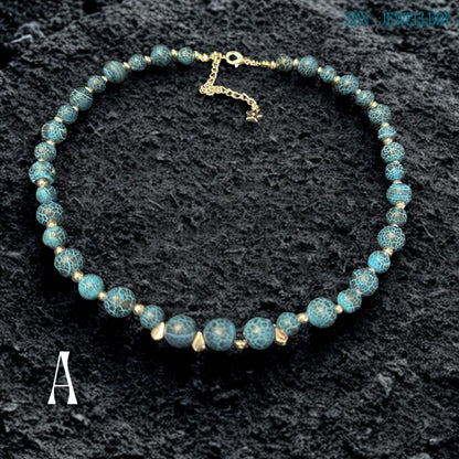 Close-up image of Blue Crackle Agate gemstone beads showing detailed crackled vein textures in deep turquoise, black, and ocean blue shades separated by polished silver spacer beads that reflect light softly against the dark background, highlighting the natural stone patterns, handcrafted jewellery construction, layered bead arrangement, and elegant celestial styling details that create a luxurious bohemian appearance.