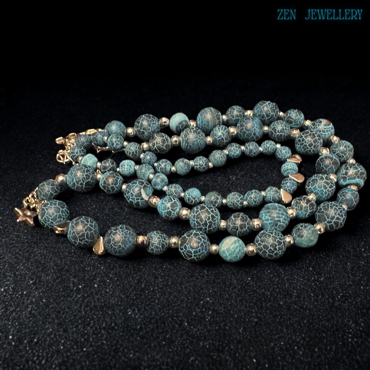 Macro close-up photograph of the Blue Crackle Agate gemstone surface revealing intricate natural crackled vein patterns across polished turquoise and black beads separated by reflective silver spacers that create a luxurious gemstone texture full of earthy character, artistic depth, and handcrafted bohemian elegance suitable for statement jewellery lovers and gemstone collectors.