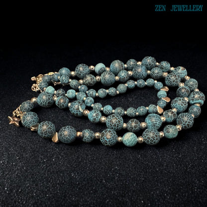 Macro close-up photograph of the Blue Crackle Agate gemstone surface revealing intricate natural crackled vein patterns across polished turquoise and black beads separated by reflective silver spacers that create a luxurious gemstone texture full of earthy character, artistic depth, and handcrafted bohemian elegance suitable for statement jewellery lovers and gemstone collectors.