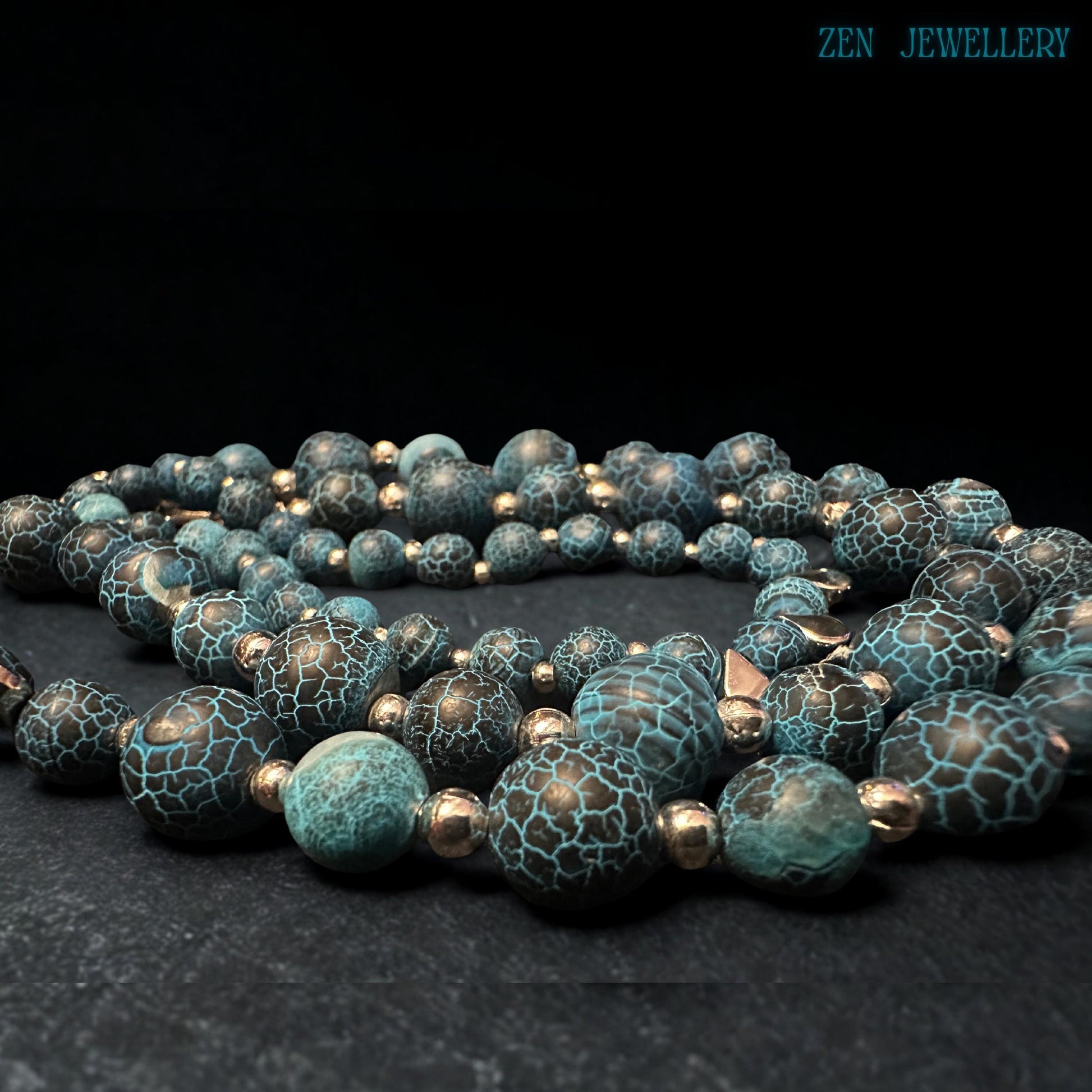 Layered gemstone jewellery set featuring Blue Crackle Agate beads arranged naturally on textured black stone creating dramatic visual contrast that enhances the turquoise crackled bead surfaces, polished silver accents, and celestial star charms while showcasing the luxurious handcrafted quality, artistic gemstone patterns, and sophisticated bohemian fashion aesthetic.