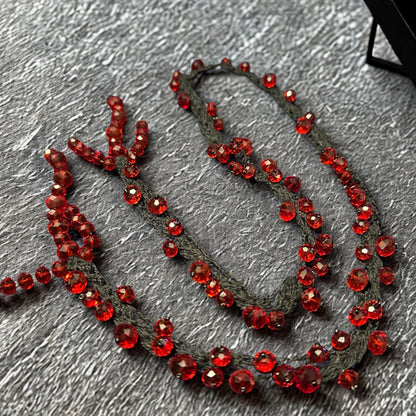 Close-up image showing detailed faceted RED CRYSTAL beads attached carefully onto black crochet strands with handcrafted precision. The rich crimson crystals vary in size and reflect warm light from multiple angles, adding glamorous sparkle and dimensional texture. The soft braided base curves naturally and enhances the organic artistic shape of the necklace. The dramatic colour contrast between red and black gives the jewellery set a luxurious g