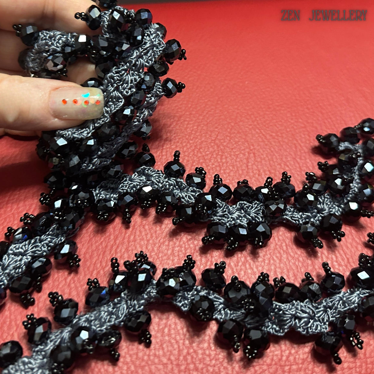 Close-up macro detail of faceted black crystals attached to intricate charcoal silk crochet lace in a handmade necklace and bracelet set. Tiny decorative bead accents surround the larger crystals, adding texture and sparkle throughout the jewellery. The handcrafted statement design combines fibre art with gemstone-inspired glamour, creating a unique wearable artwork piece for women who love bold accessories and dramatic jewellery styling.
