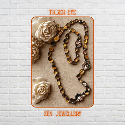 Elegant TIGER EYE necklace and bracelet set featuring polished brown, honey, and caramel gemstone beads with shiny gold spacer beads and delicate gold chain details. The smooth tiger eye stones reflect warm natural light beautifully and create an earthy luxury appearance styled on a soft marble background with dried flowers for a romantic boho aesthetic.