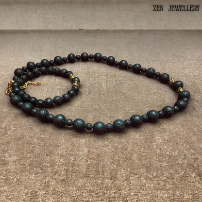 Matching lava stone bracelet shown with matte black volcanic beads and decorative gold spacer accents. The porous natural lava stones create an earthy bohemian aesthetic, while the polished golden details add elegance and sophistication. The bracelet fits comfortably on a beige background and pairs beautifully with the coordinating necklace for a timeless handcrafted jewellery set.