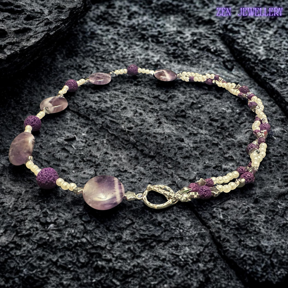 Handcrafted purple gemstone-style beads are paired with textured lava stone accents and tiny white pearl beads to create a feminine statement necklace. The polished surfaces reflect light beautifully while maintaining a soft romantic appearance suitable for casual or evening wear.