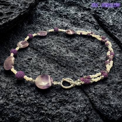 Handcrafted purple gemstone-style beads are paired with textured lava stone accents and tiny white pearl beads to create a feminine statement necklace. The polished surfaces reflect light beautifully while maintaining a soft romantic appearance suitable for casual or evening wear.