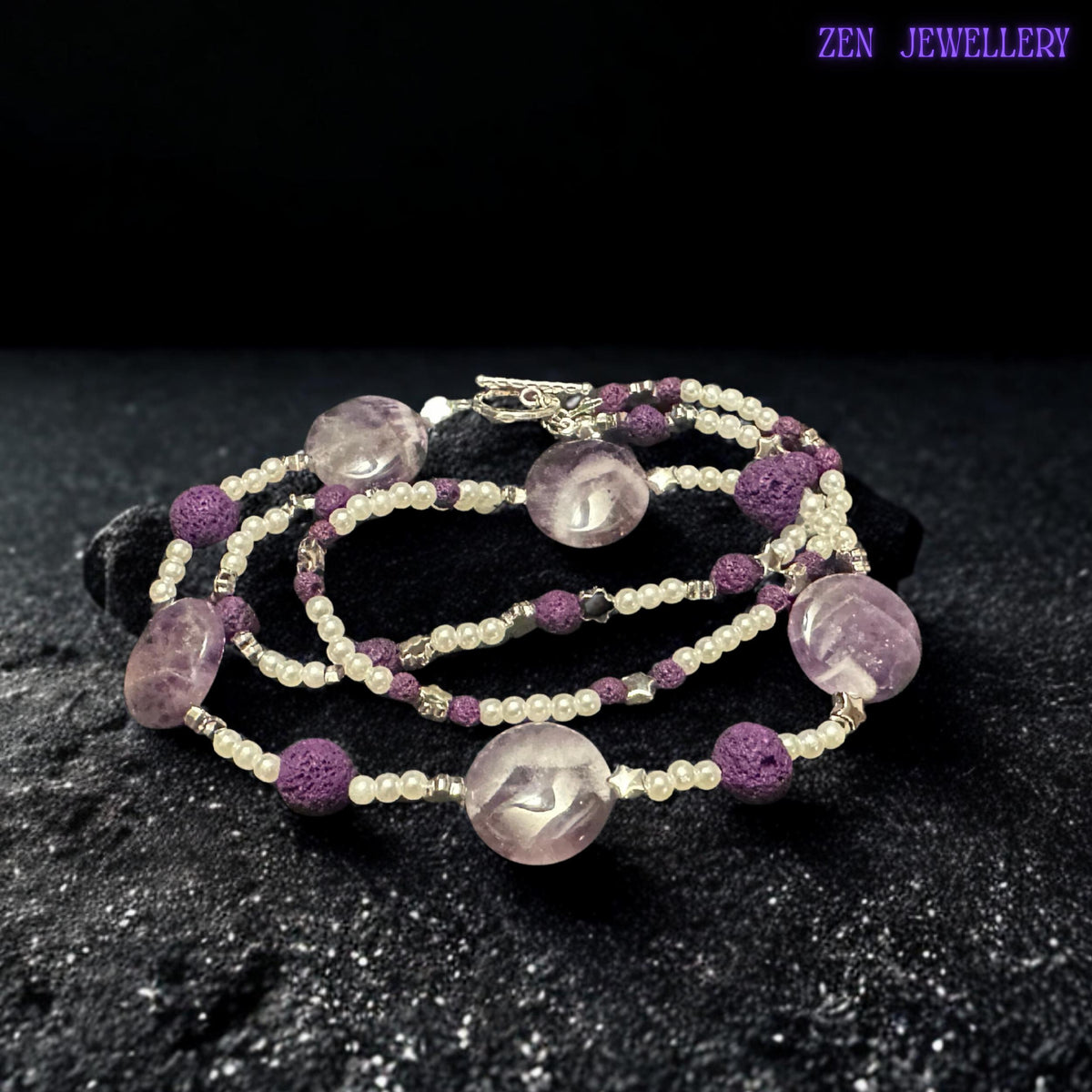 This amethyst-inspired necklace combines polished lavender beads, textured lava stones, silver accents, and delicate pearl-style spacers in a balanced handmade design. The artistic arrangement creates a lightweight statement necklace full of texture and feminine charm.