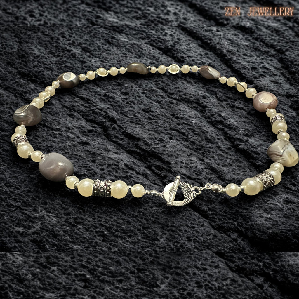 Handmade BOTSWANA AGATE necklace shown in detailed close-up revealing polished striped agate stones paired carefully with creamy pearl beads and silver decorative spacers. The natural gemstone variations create earthy elegance while the silver chain and toggle clasp add vintage-inspired texture and shine. The balanced arrangement of gemstones and pearls creates softness, contrast, and timeless bohemian style.