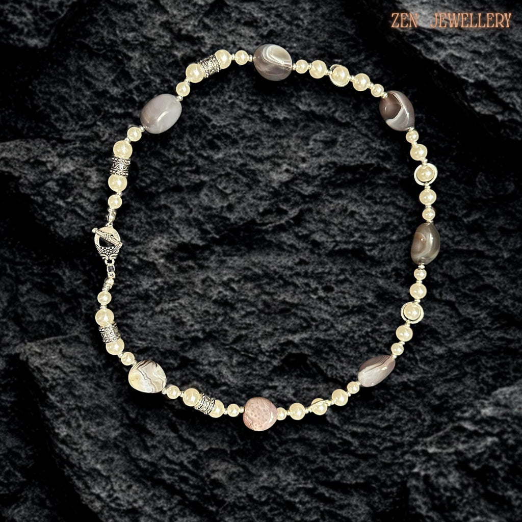 Handmade BOTSWANA AGATE statement necklace photographed on a textured black background to emphasise the elegant neutral colour palette and polished gemstone surfaces. Large oval agate beads create earthy visual depth beside creamy pearl strands while silver rhinestone spacers add delicate shine and luxury detail. The layered artistic composition feels balanced, lightweight, and feminine with timeless bohemian elegance.