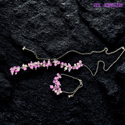 Handmade floral-inspired gemstone necklace displayed with coordinating bracelet and earrings on a dark stone-textured surface. The jewellery combines pastel pink, lavender, lilac, and pearl white beads attached to delicate silver chain strands for a romantic feminine look. Clustered bead arrangements create natural movement and artistic texture while reflective silver details add soft sparkle. Small pearl-like accents provide contrast and eleganc