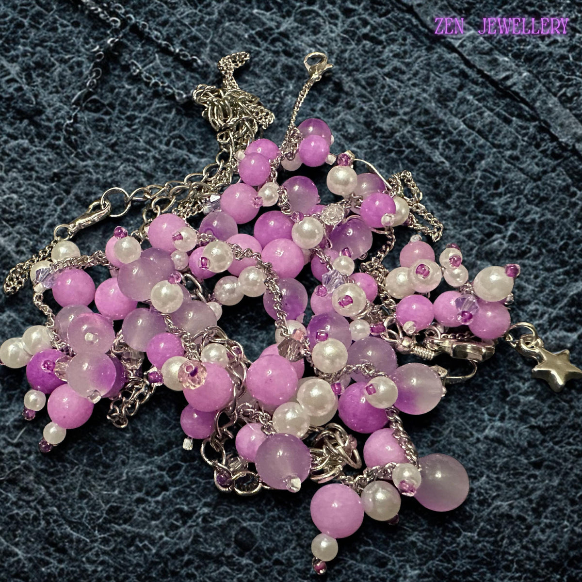 Pastel gemstone jewellery collection featuring a statement necklace, bracelet, and dangling earrings made with soft pink, lilac, pearl white, and lavender beads attached to elegant silver chains. The clustered bead design creates layered movement and artistic texture while polished gemstone surfaces reflect light softly. The jewellery feels feminine, romantic, and lightweight with floral-inspired detailing and delicate metallic accents throughout