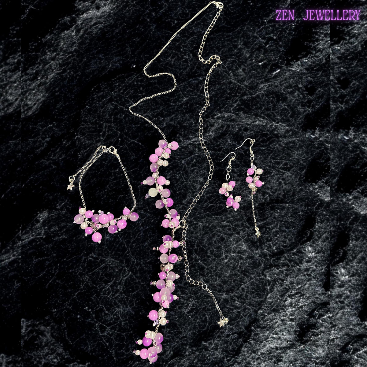 Long pastel gemstone necklace with silver chain details featuring clustered glossy beads in blush pink, soft lilac, pearl white, and lavender tones. The necklace creates elegant cascading movement with asymmetrical bead placements and delicate silver spacers that reflect light softly. Matching bracelet and dangling earrings complete the coordinated boho jewellery set. The design feels romantic, artistic, lightweight, and feminine with floral-insp