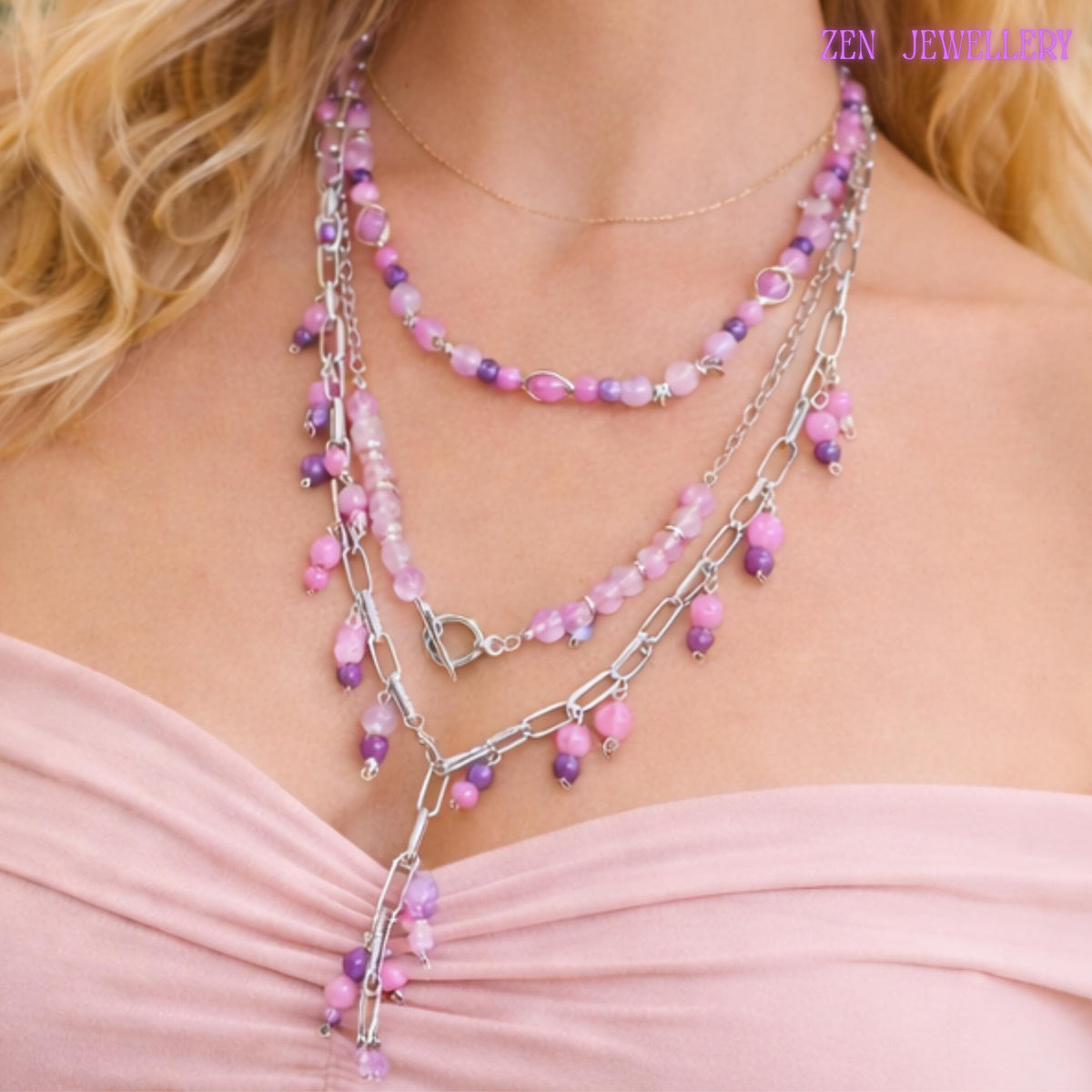 Layered pastel gemstone necklace featuring three silver chain strands decorated with pink, lilac, lavender, and purple bead clusters attached along chunky metallic links. The necklace combines polished round gemstone beads with faceted crystal accents for subtle sparkle and luxurious detail. Small dangling bead charms create movement while the silver toggle clasp becomes part of the decorative front design for a modern handcrafted finish.