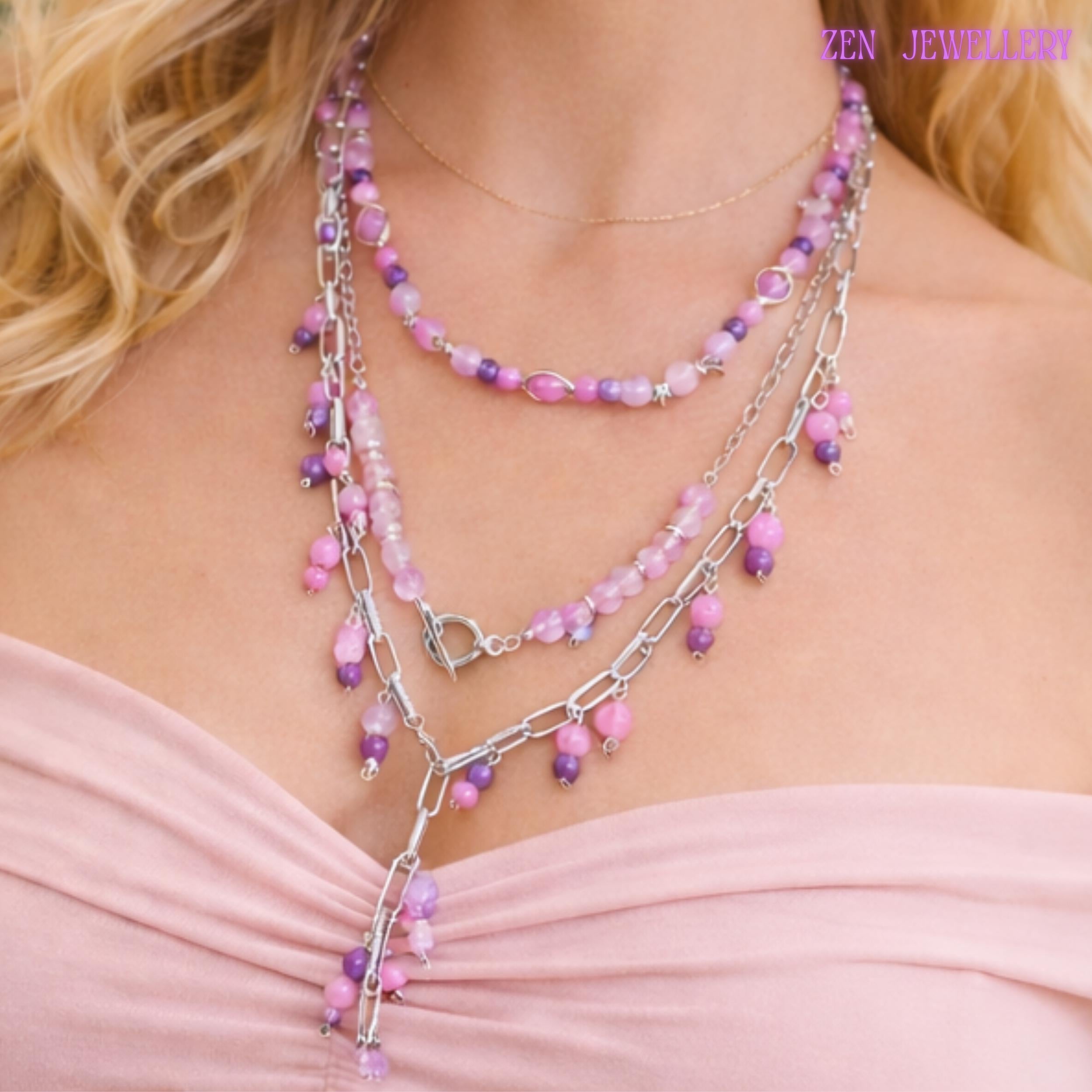 Layered pastel gemstone necklace featuring three silver chain strands decorated with pink, lilac, lavender, and purple bead clusters attached along chunky metallic links. The necklace combines polished round gemstone beads with faceted crystal accents for subtle sparkle and luxurious detail. Small dangling bead charms create movement while the silver toggle clasp becomes part of the decorative front design for a modern handcrafted finish.