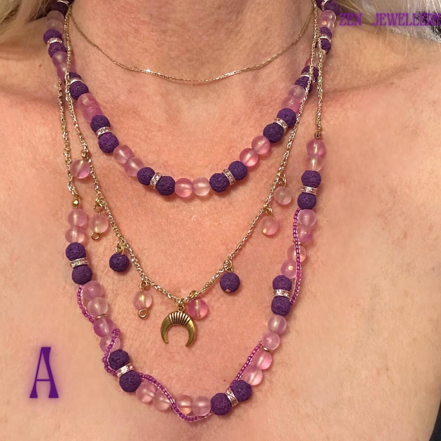 • Artistic flat-lay image showing the complete layered necklace arrangement with delicate dangling pink bead charms suspended from a fine golden chain strand. The soft translucent blush beads create a glowing appearance while the textured volcanic purple stones add depth and contrast. The dark embossed background enhances the luxurious gold details and highlights the elegant handcrafted movement within the layered necklace structure.