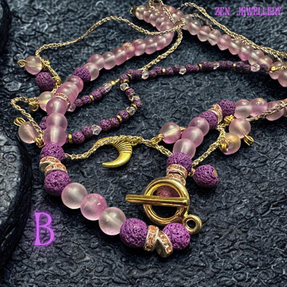 • Detailed image capturing the texture of the matte purple lava stone beads contrasted beside glossy translucent blush pink gemstone beads. The volcanic style beads feature an earthy porous surface while the pink beads appear smooth and luminous. Gold spacer rings add refined sparkle between each section creating balance between mystical bohemian texture and elegant feminine shine.