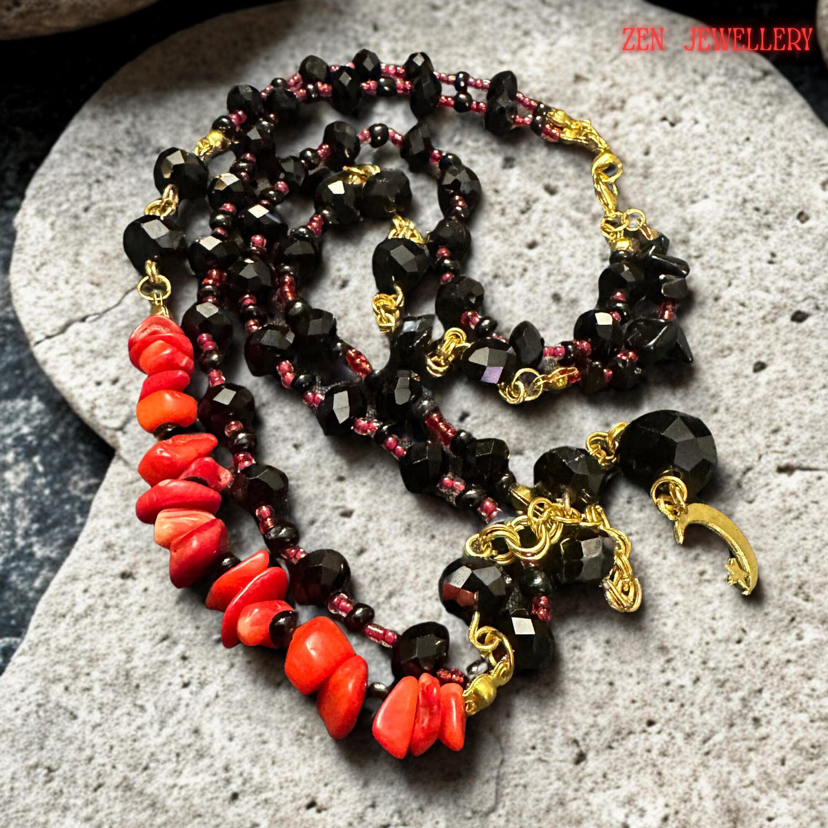 Artistic close-up image focusing on the faceted black crystal beads and red coral chips positioned along the front strand of the necklace. Gold chain details and metallic connectors create elegant contrast while the moon pendant adds celestial charm to the handmade jewellery design. The necklace combines bohemian style with modern sophisticated fashion.
