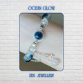 Elegant BLUE GEMSTONE bracelet displayed on a shimmering water-inspired background, featuring deep ocean-blue gemstone beads paired with transparent crackle crystal beads that reflect light beautifully. A silver-framed blue gemstone focal charm sits at the centre, enhanced by delicate silver star details and flowing chain accents. The bracelet measures 19 cm (7.48 inches) and features an adjustable fit for comfortable everyday wear.