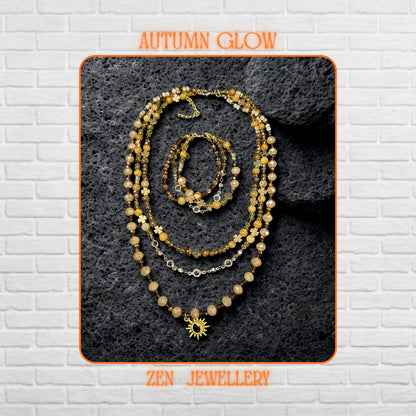 A layered boho necklace and bracelet set featuring warm earth-tone crystals and a gold sun charm on a textured stone background.