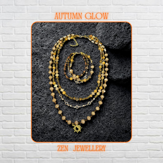 A layered boho necklace and bracelet set featuring warm earth-tone crystals and a gold sun charm on a textured stone background.