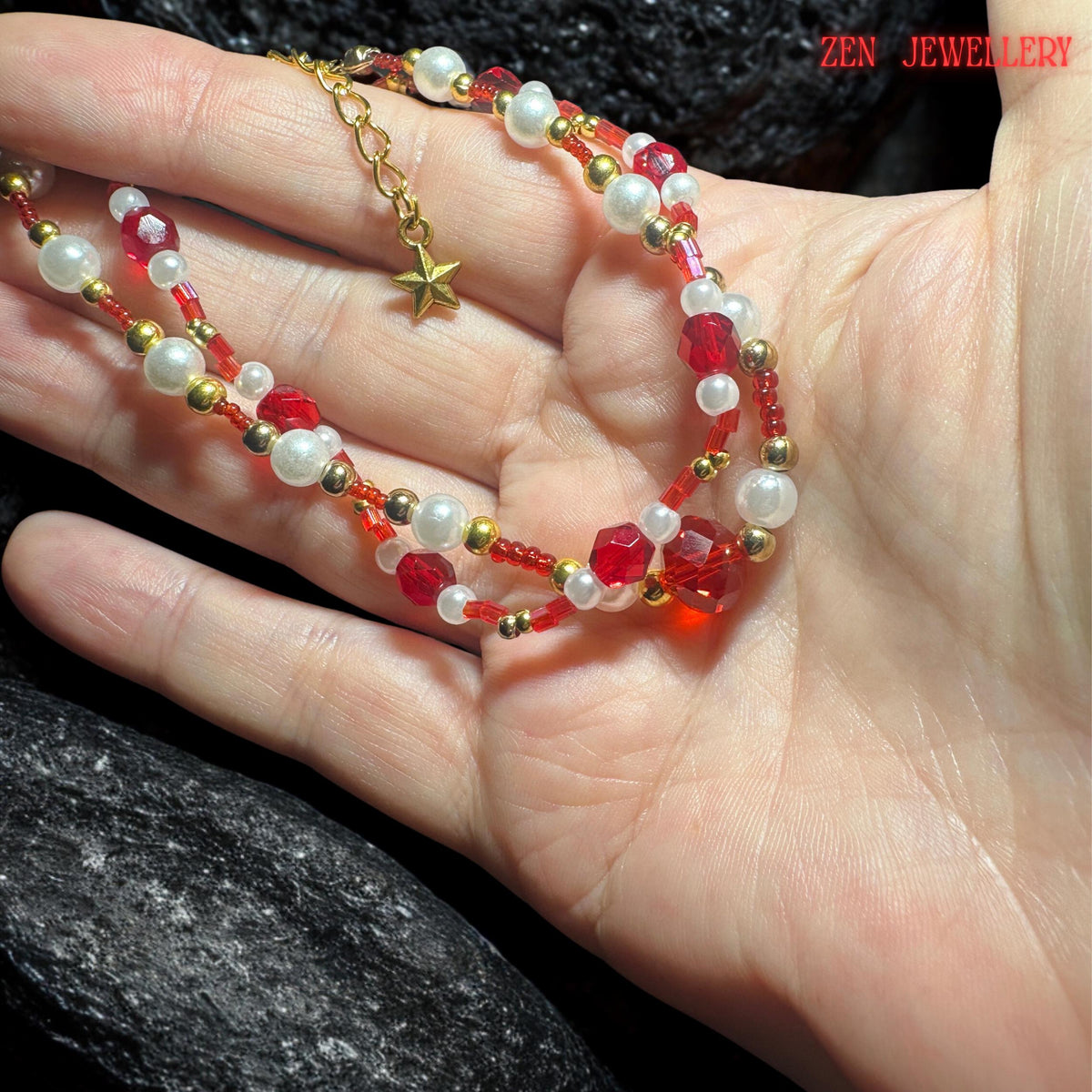 Handmade layered jewellery set photographed from above to show the arrangement of double necklace strands and matching bracelet against a dark stone background. The design combines coastal jewellery inspiration with romantic bohemian styling through the use of red crystals ivory beads gold details and the delicate starfish pendant focal point.