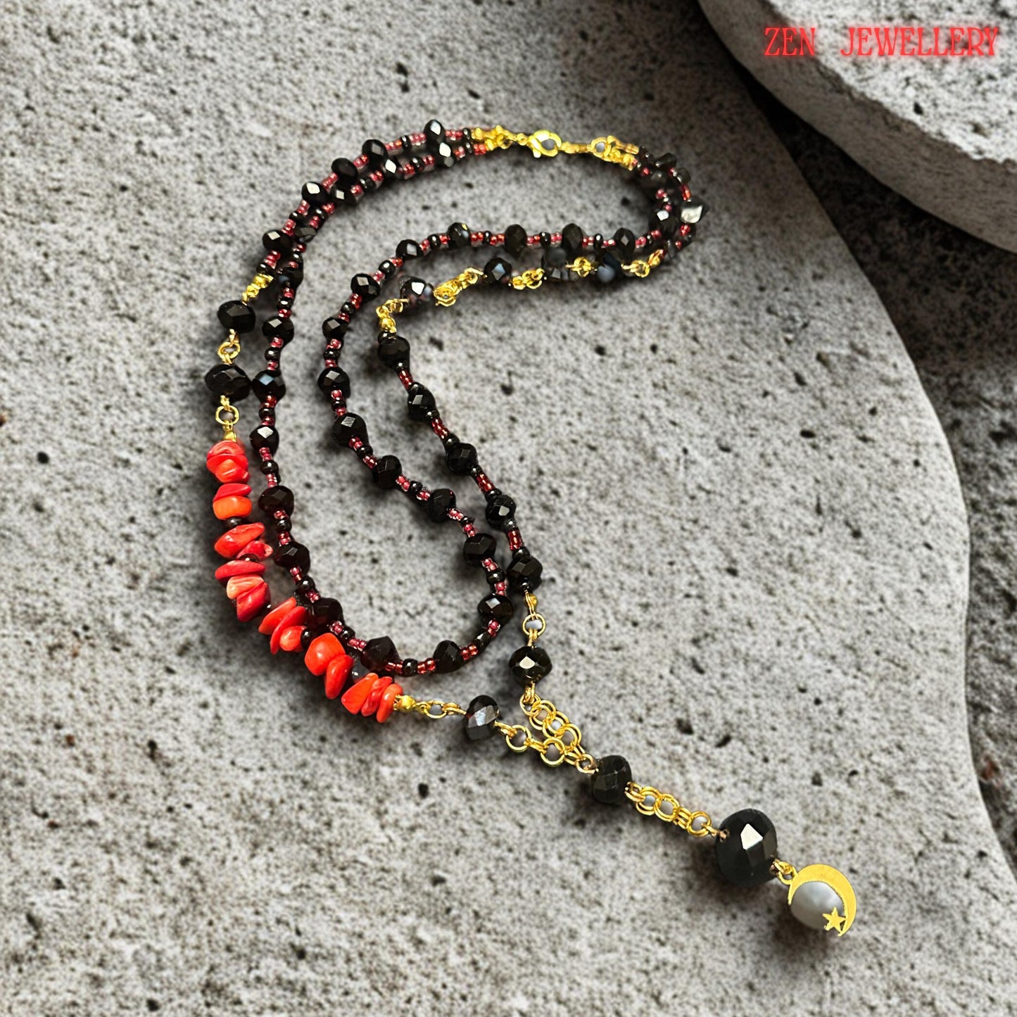 Handmade black crystal jewellery necklace displayed with layered strands and geometric black beads surrounding a gold crescent moon pendant. The glossy faceted beads reflect light beautifully while the red coral accents provide warmth and vibrant colour contrast. The sophisticated layered design gives the necklace an elegant statement appearance, perfect for evening outfits and artistic fashion styling.