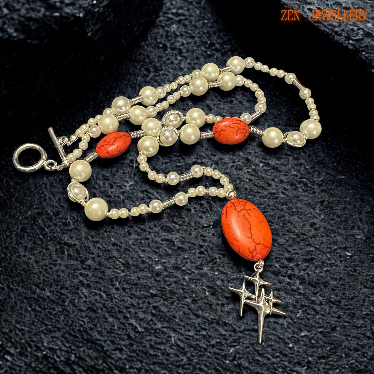 Detailed product image of handmade pearl and coral necklace highlighting the natural crackle texture of the large oval red gemstone pendant and the polished silver star charm suspended below. Smaller matching coral-effect beads are positioned symmetrically on each side creating balance and refined artisan craftsmanship throughout the jewellery design.